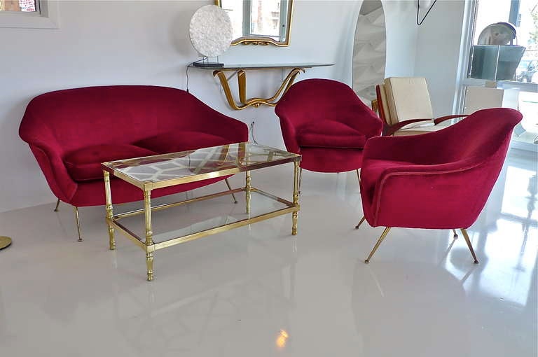 Uber chic 1950's Italian salon suite consisting of a pair of lounge chairs and love seat sofa.  All with loose down filled seat cushions and solid brass legs. Upholstery, though not the original, is vintage red velvet. Sexy lines and comfy as well.