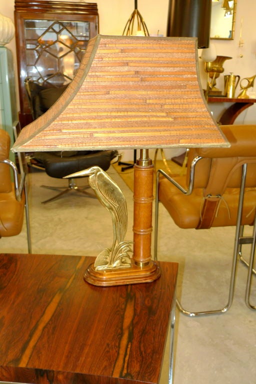 In the style of Maison Charles and Jacques Adnet this lamp has an extraordinary woven brass framed shade atop a main column of faux bamboo sharing its base with a brass heron.
