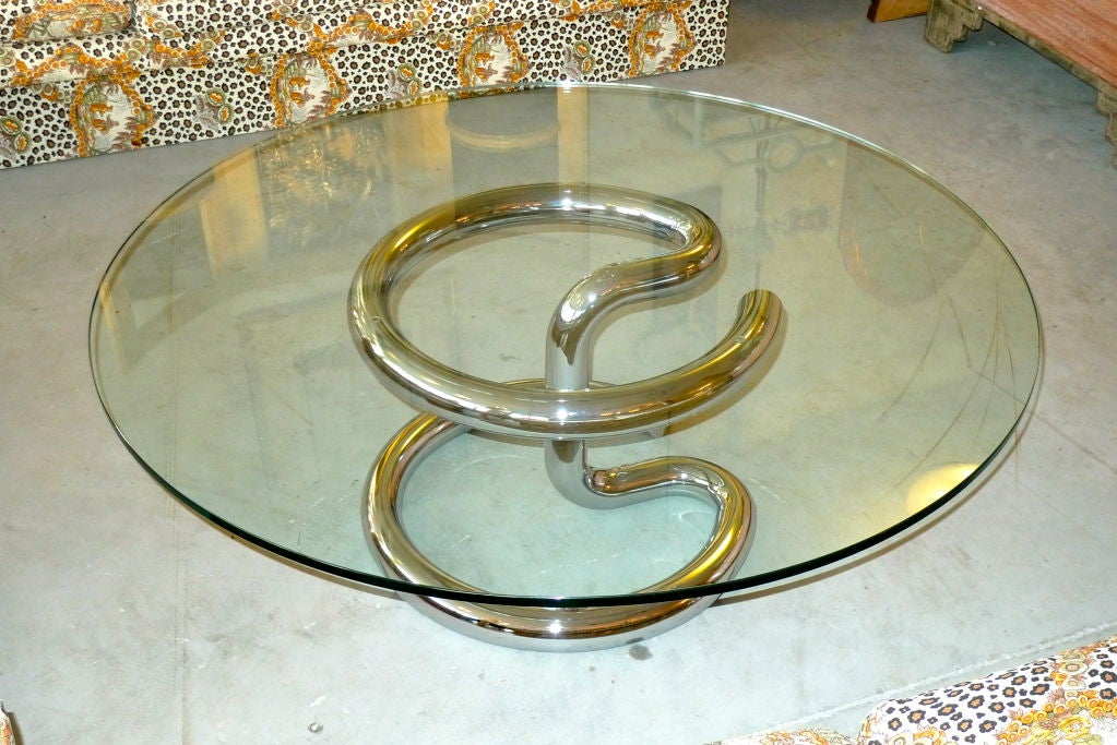 Playfully beautiful round coffee table by Paul Tuttle in thick tubular chromed steel with a 47 inch glass top (1/2 inch thick smooth edge glass). Early 70's pop art mod with  fluid sculptural metal knot.

Diameter of base is 22 inches so it is