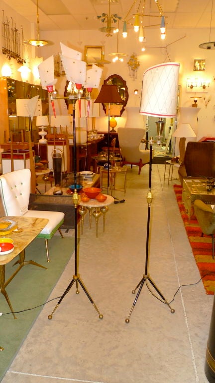 Pair of early 1950's French floor lamps identical from the waist down with brass ball tripod legs and feet. Above the shoulders the one on the left is an homage to Pierre Guariche with four radiating arms holding torch lights as well as one as the