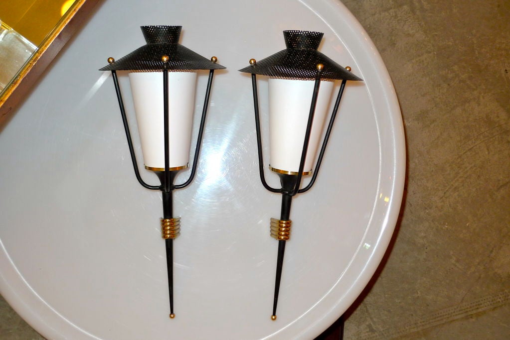 A matching pair of French 1950's tochere lantern sconces produced by Arlus, design attributed to Mathiue Mategot.

Matte black enamel and polished brass wall mounts.