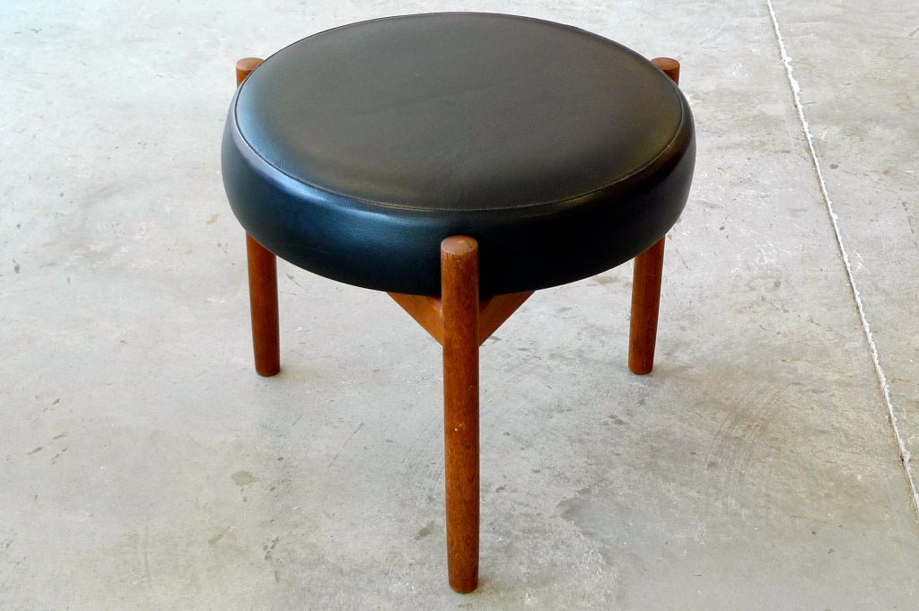 A handsome vintage Danish round ottoman or foot stool. Teak three legged frame and black leather upholstery on round cushion. Stamped Spøttrup. Made in Denmark