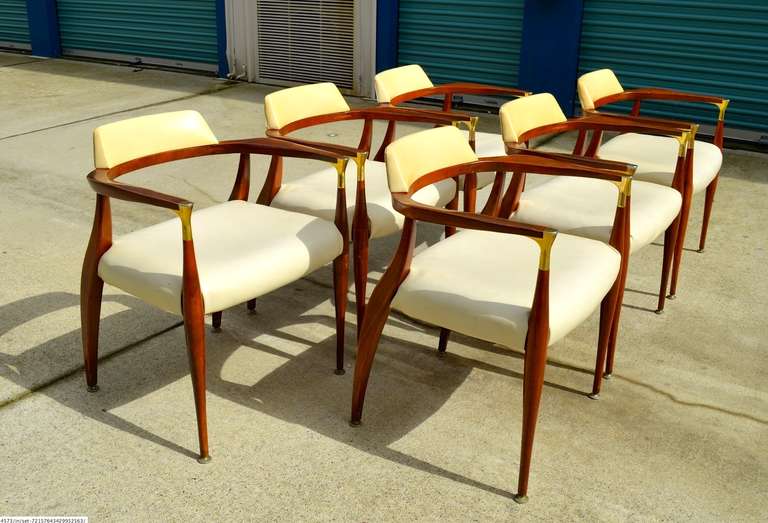 Unusual dining chairs by Bert England with modernist horseshoe form with curved backrest cushion and walnut sculptural frame and brass embellishments at the front of each arm.  Upholstery is the original faux leather so it should be