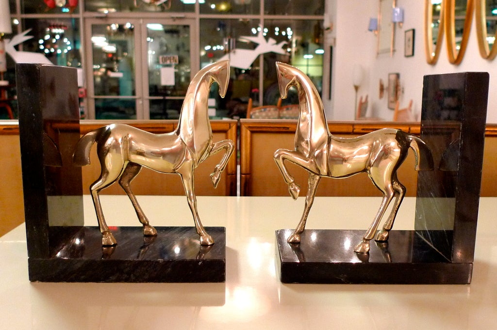 Handsome pair of Hollywood Regency bookends made from graphite black marble and stylized cast brass horses in the Etruscan form.  In the manner of Frederick Weinberg and Fantoni