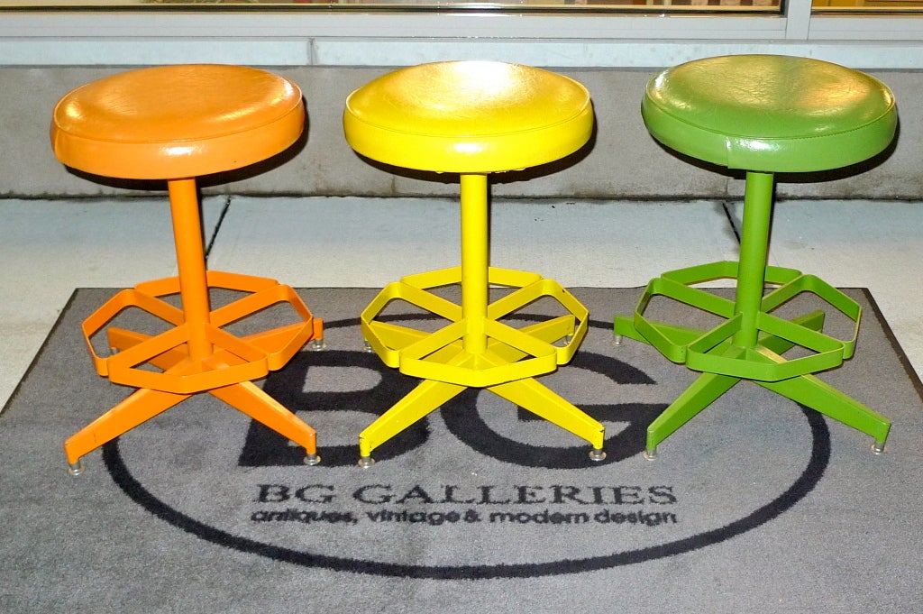 Colorful mid-century swivel stools made of industrial steel painted orange, green and yellow with round textured vinyl covered seat cushions.  Seat swivels 360 degrees.  Original 