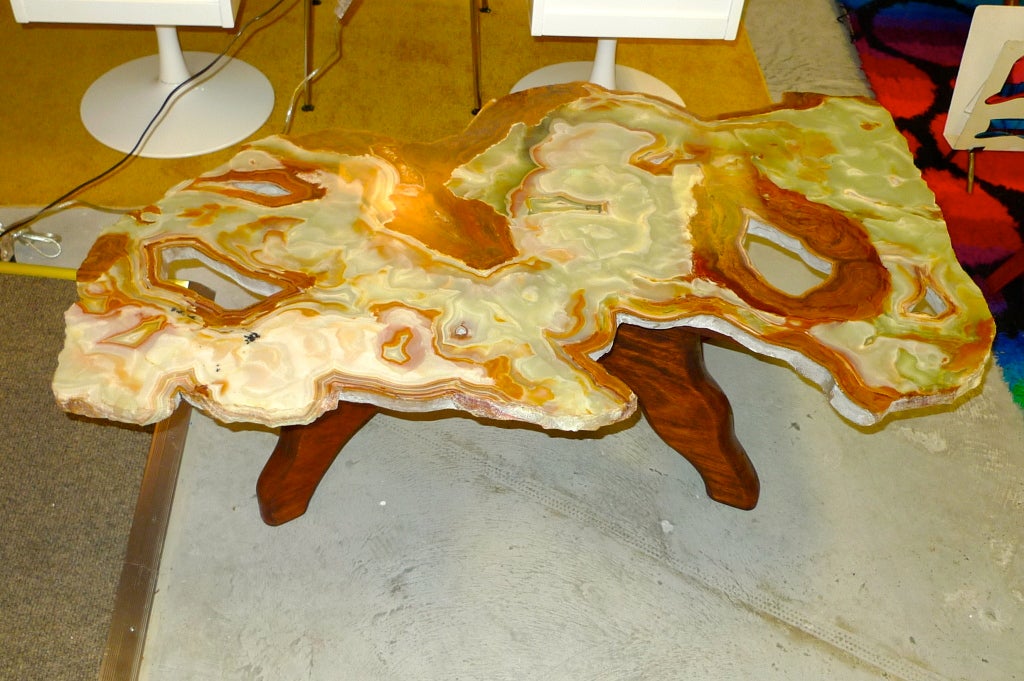 Cocktail table consisting of an organic free-form one inch thick slab of polished Madagascar agate mineral which sits atop an primitive X form base of solid walnut with legs in wavy form to complement shape of agate slab. Agate has several natural