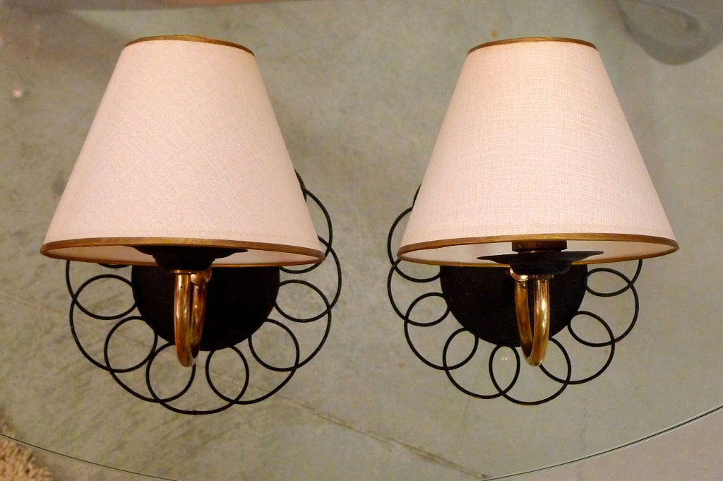 Enchanting petite sconces from 1950's France in the style of Jean Royere consisting of a blackened metal disk with an outer ring of scrolling and looping blackened wire with curved brass rod terminating in a single candle bulb socket.

We have only