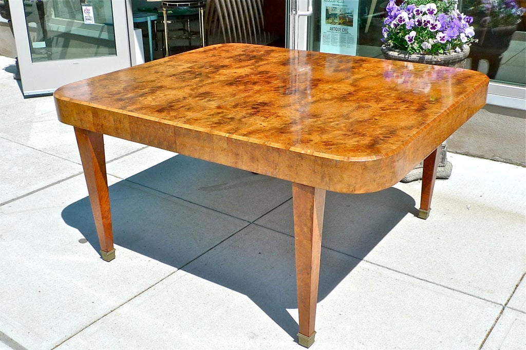 French Art Deco burl walnut dining table in square form with rounded corners and chamfered edge above apron.  Squared tapering legs have bronze caps.

The original leaf is missing so a 30