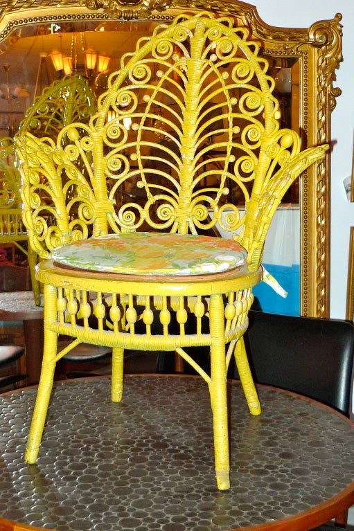 A sweet mini-peacock style yellow painted wicker chair with fiddelheads.  Woven seat has been replaced with plywood and a loose cushion for more firm support.