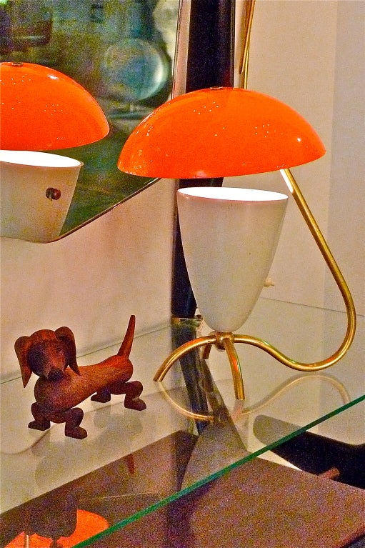 Merry little Italian table lamp from the 1950's with a brass tri-pod base and an enameled Arteluce style uplight cone with an acrylic orange dome as reflector.