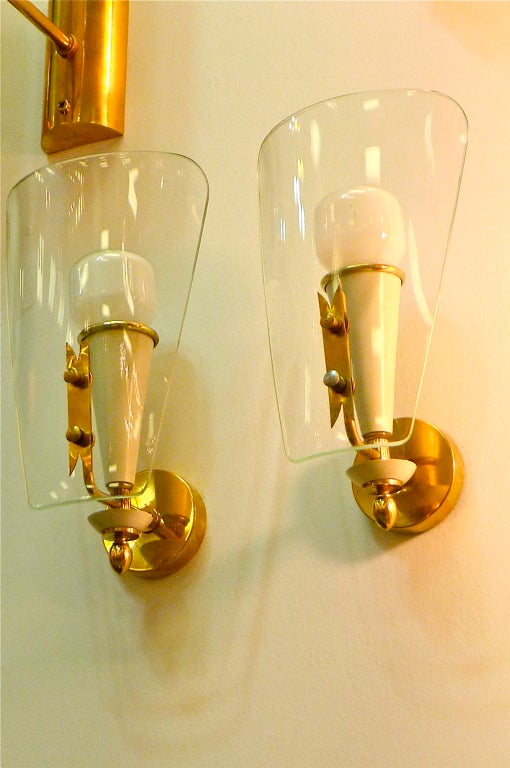 Enchanting pair of early 1950's sconces in the manner of Pietro Chiesa for Fontana Arte made of curved clear glass, brass and ivory enameled aluminum.

Currently wired for E14 candelabra bulbs up to 75 watts each.

Backplate is 2.5 inches diameter.