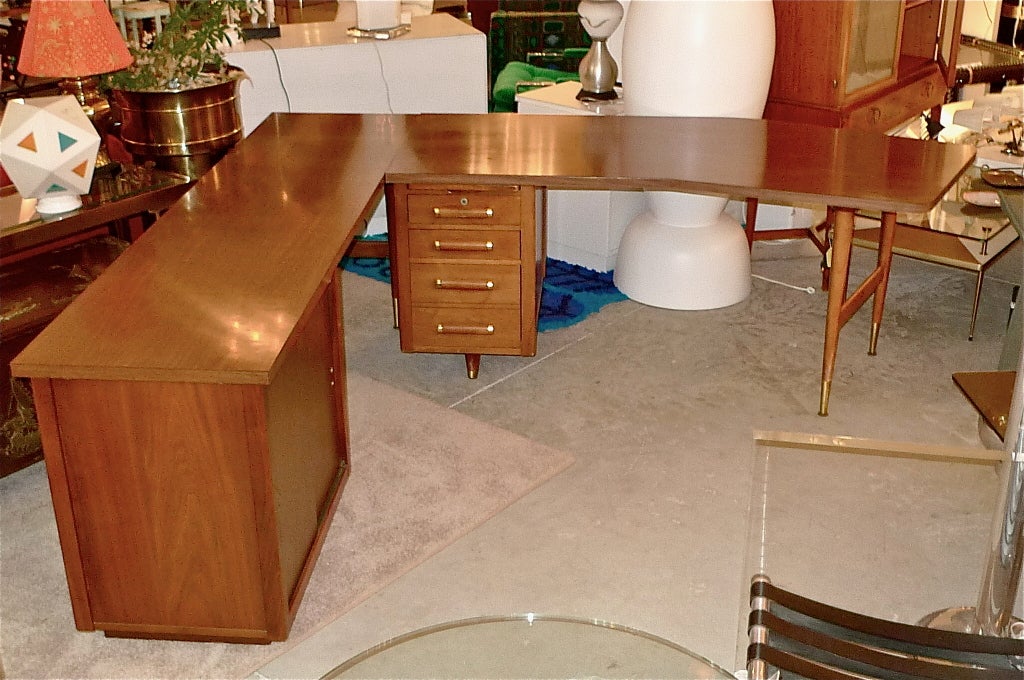 American made to the Italian modernist taste, two piece office suite. Desk with boomerang shaped top, tapered slim legs with brass sabots and feet, file drawer, two standard drawers and pull-out writing surface. Credenza consists of a rectangular