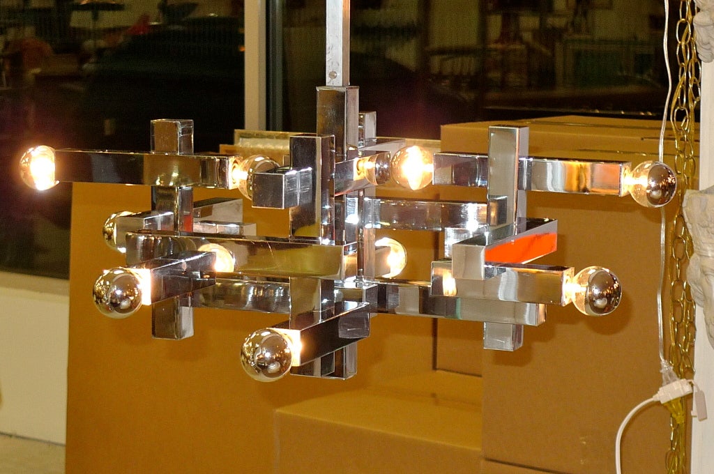 A dramatic and sculptural chandelier by Gaetano Sciolari in square chromed steel intersecting on multiple levels and planes, creating mass with the void of space.

10 sockets for candelabra screw cap bulbs up to 60 watts each.  Shown with chrome
