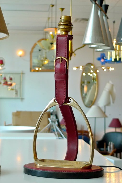A thoroughbred French 1950's lamp by Longchamps Paris for your writing table. A solid brass stirrup mounted and wrapped in saddle-stitched leather with brass buckle. Frequently attributed to Jacques Adnet for Hermes.  Color of leather is burgundy. 