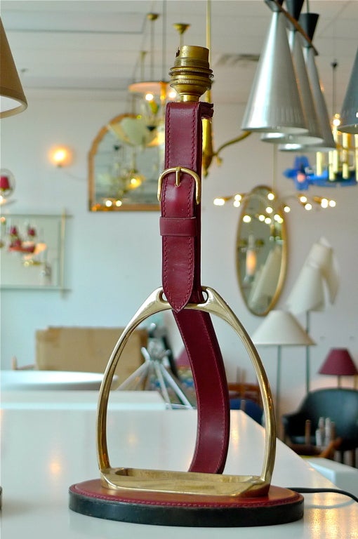 Une lampe française pur-sang des années 1950 par Longchamps Paris pour votre table à écrire. Un étrier en laiton massif monté et enveloppé dans du cuir cousu à la selle avec une boucle en laiton. Fréquemment attribué à Jacques Adnet pour Hermès.  La