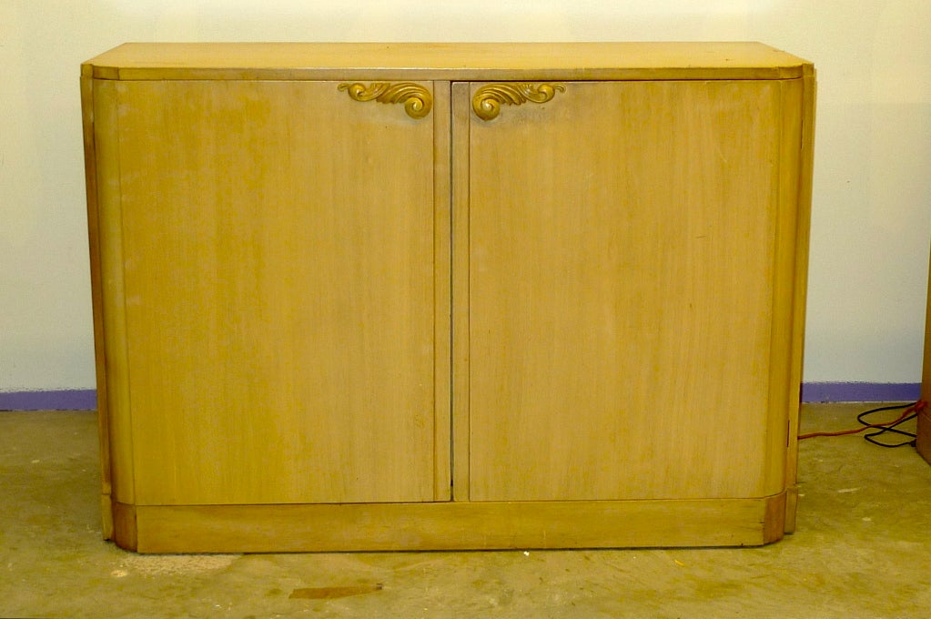 Early 1940's sideboard or linen press by Lorin Jackson for Grosfeld House.  Two banks of four open drawers behind double doors. Carved foliate handles and curved notched corners.  
This is in its original finish which is faux grain painted light