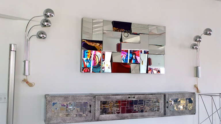 A long and slim wall mounted console cabinet in immaculate condition very much in the style of Paul Evans (and Marvin Arenson) clad in repousse aluminum and chromed steel tiles, having three doors which conceal open storage compartments.  Left and