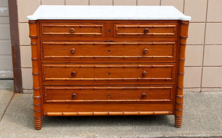 A lovely cognac color French faux bamboo commode with original white marble top. Three large drawers and two top smaller drawers with a central lock in between them. 