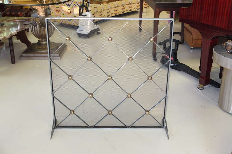 Mid-century modern fireplace screen. Square bare steel frame with diamond shaped lattice pattern on front with wire mesh. Rounded brass caps at the intersection of lattice pattern. Angled aluminum footings on both sides. Styling evocative of the