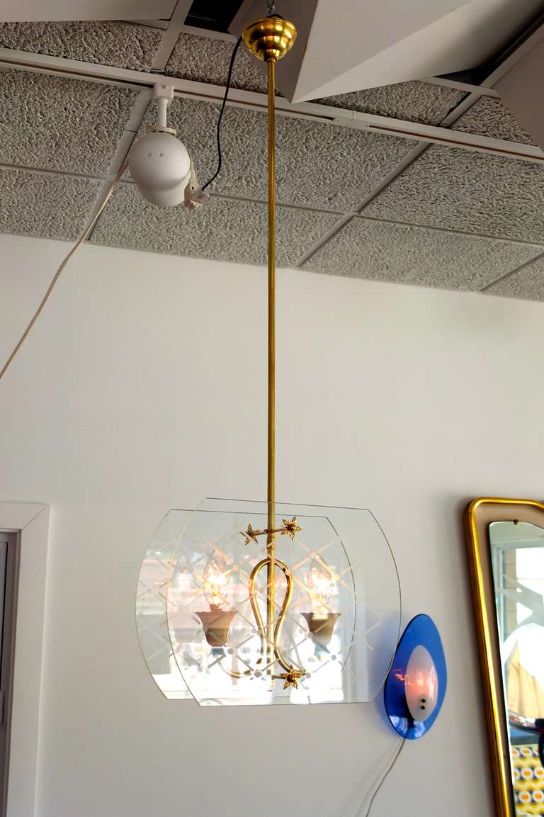 1940's Italian pendant lantern in the style of Pietro Chiesa for Fontana Arte.  Elegantly scrolled brass terminating in two scallop edged tulip form aluminum socket cups in original ivory enamel floating between two cushion shaped panes of glass