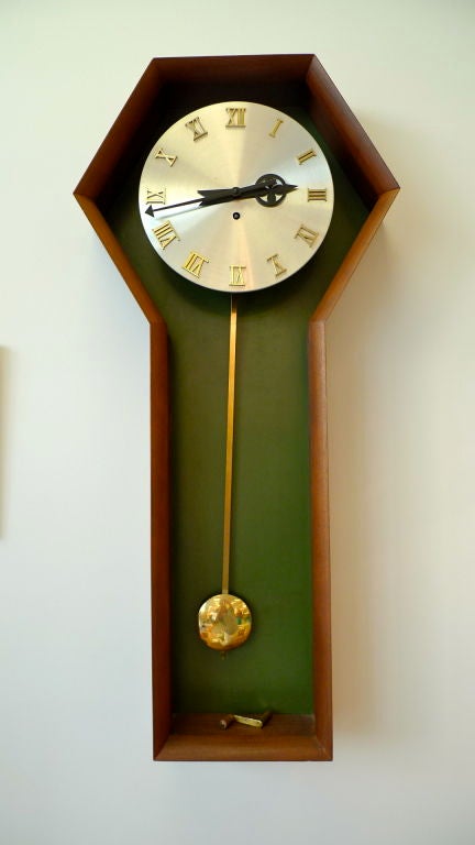Brushed metal face, gold Roman numerals, black hands, brass pendulum and key in coffin shaped walnut case by George Nelson for Herman Miller. Green laminate back.