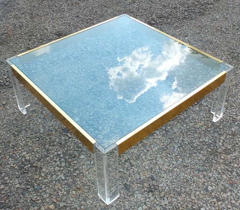 Immaculate and chic cocktail table, square with Lucite cornered legs, brass anodized aluminum frame and flush plate glass top.