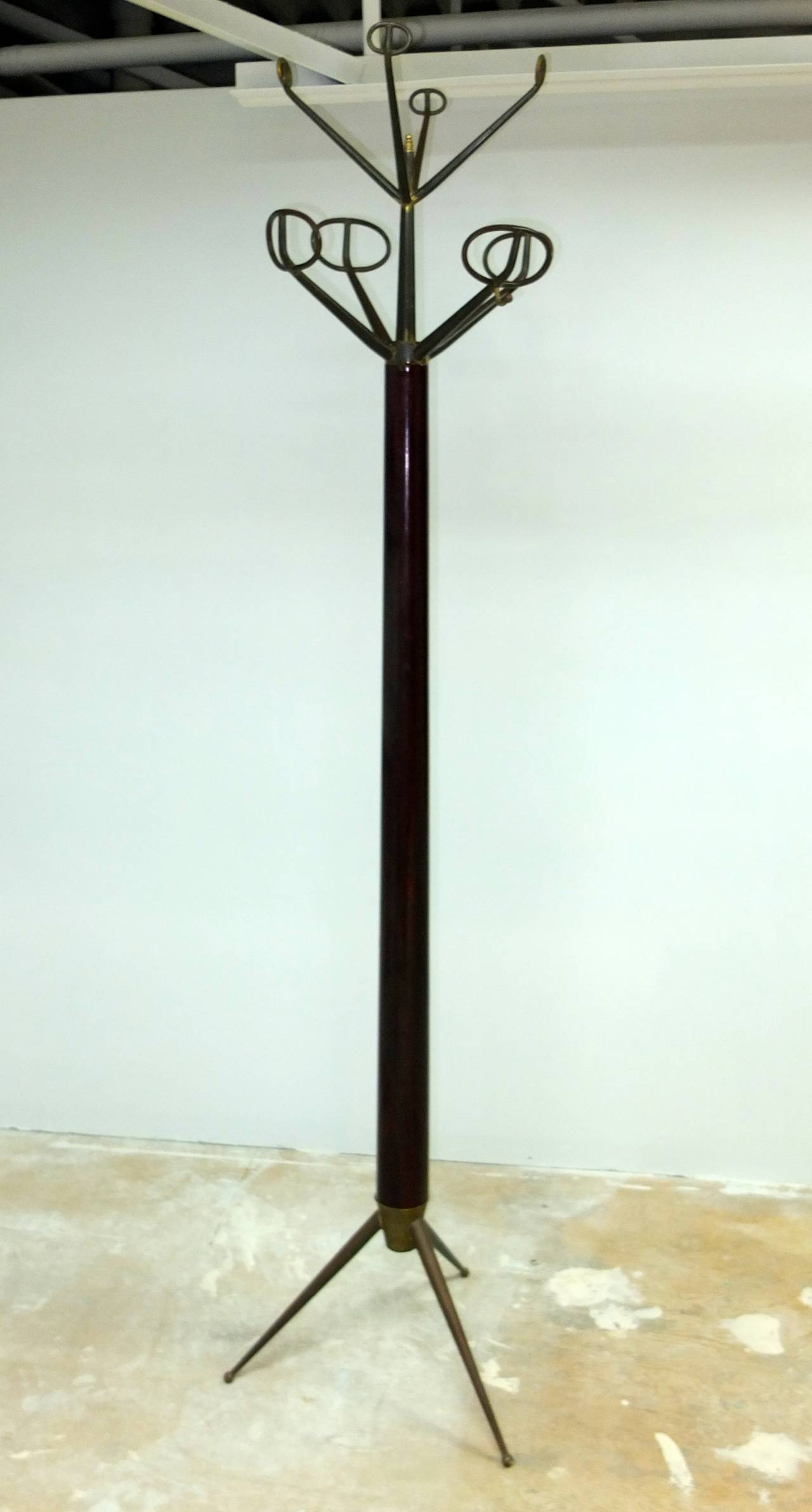 Stunning 1950s Italian coat stand with a single mahogany tapered shaft set in a solid brass tapered tripod base and topped with a two-tier crown of solid brass tapered hooks with modernist loop ends. We have chosen to leave the heavy bronze colored