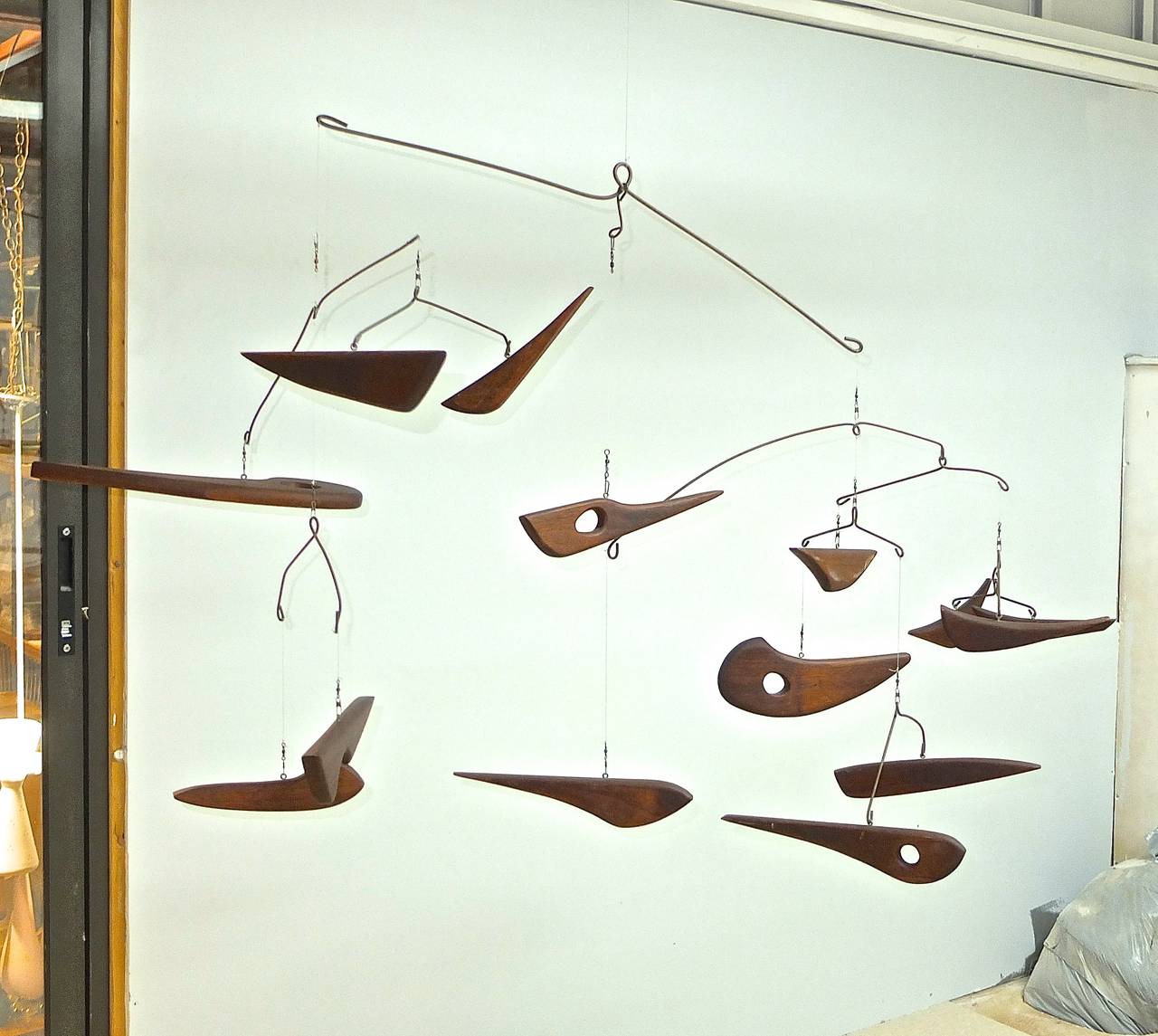 Mid-20th Century mobile consisting of fourteen abstract walnut wood forms suggesting fish suspended on monofilament from arched metal mounts. Height 35