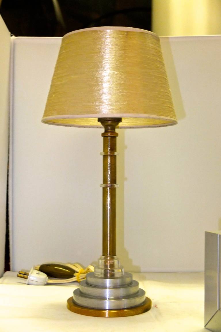 A French art deco table lamp by Hubens, Model 4520 from the 1937 catalog. Bronze body on stacked disk base of aluminum and bronze with clear lucite embellishments.  

Originally this would have had a spun aluminum flared cone shade to direct the