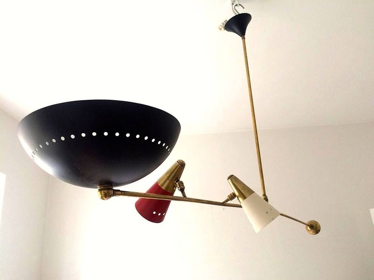 Minimalist and linear pivoting counter-balance pendant light one large black enameled dish reflector which faces up or down plus two articulating cones with brass caps and enameled white and red. Ceiling canopy enameled black. In the style of Angelo
