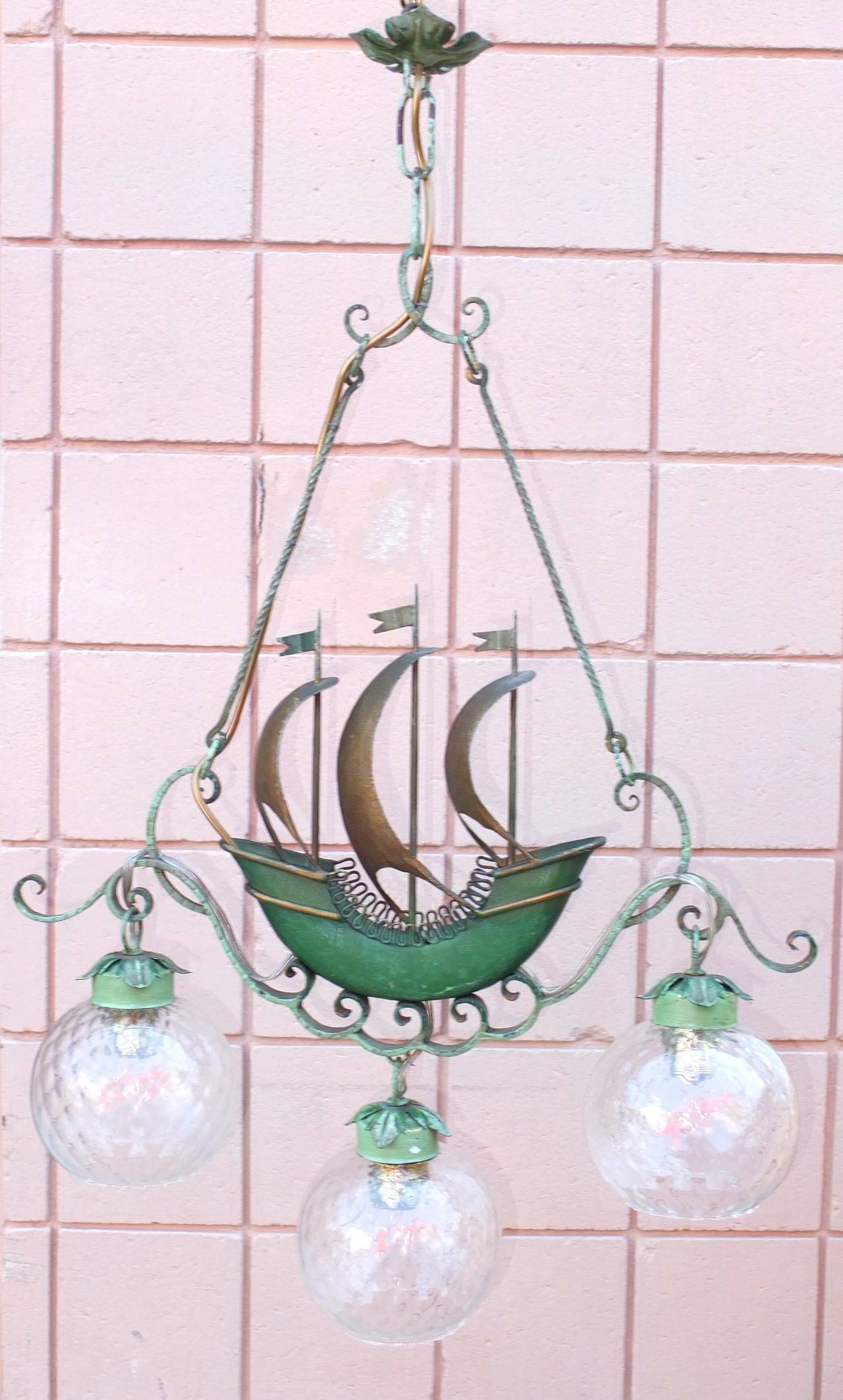 Lovely vintage 1940's Italian chandelier with original green painted tole and wrought iron framing a model of an 18th century three masted merchant ship.

Three glass globes each hold one standard size Edison screw cap bulb.

If desired for