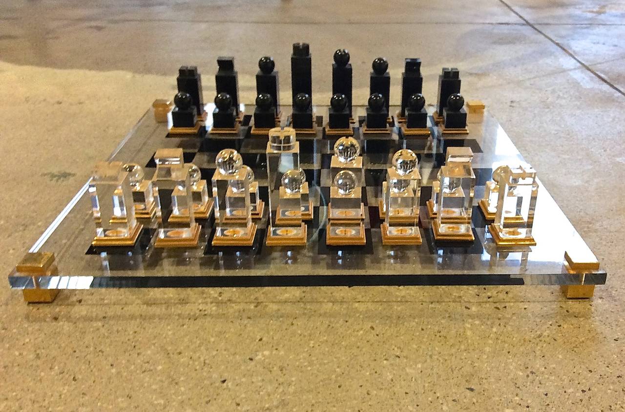 Vintage chess set by Michel Dumas. 

Largest piece is 4 inches high.  Pawns are 1-3/4 inches.  Chess board is glass with gilt brass standoffs,  17-1/2 inches by 17-1/2 inches.  Chess pieces are opaque black and clear lucite with 24k accents.