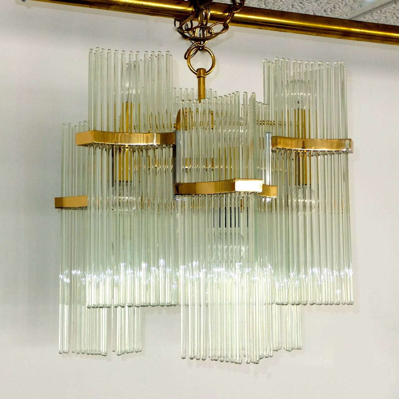 Glamorous 1970's chandelier by Gaetano Sciolari for Lightolier.  Substantial polished brass frame with six staggered triangular form clusters of suspended 16 inch glass rods which produce a blingy ambiance.  The 12 bulbs (60 watts each) provide