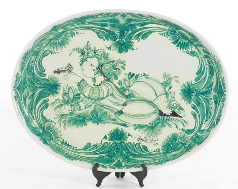 Large majolica glazed ceramic oval platter with tall sides, hand decorated in green and black on white with a figure and a bird surrounded by foliate designs, signed and dated '73, together with a custom made low table base with four tapering legs,