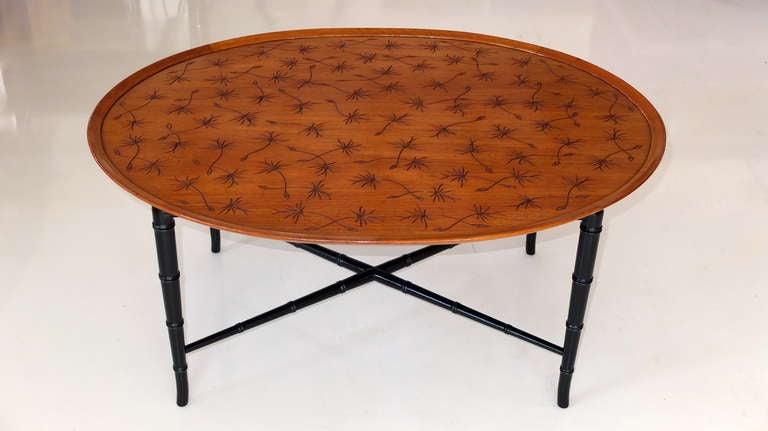 An elegant oval mahogany coffee table by Kittinger. The tray-like top has a raised edge, the center of which has been incised with naturalistic windswept thistles. The top is supported by ebonized bamboo form legs, connected with an X stretcher. 
