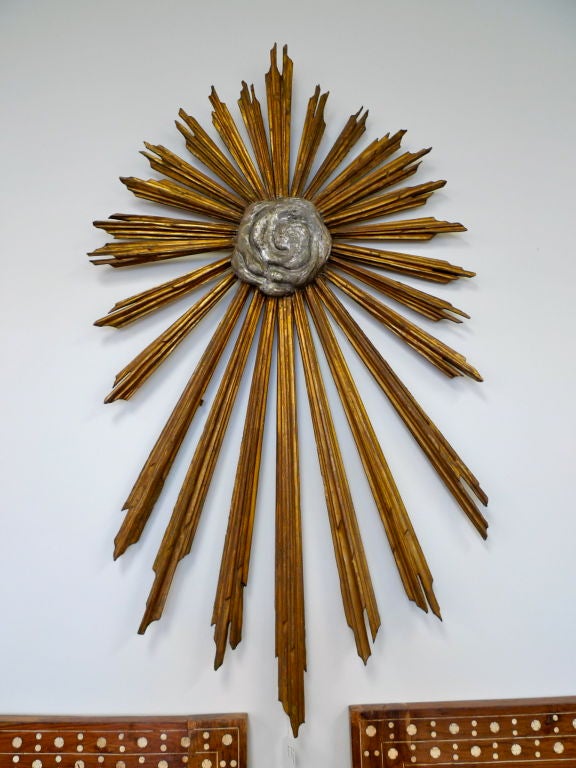 A 18th century Italian carved gilt wood religious sunburst with beams radiating from a center silvered gesso cloud like formation representing the Holy Spirit.