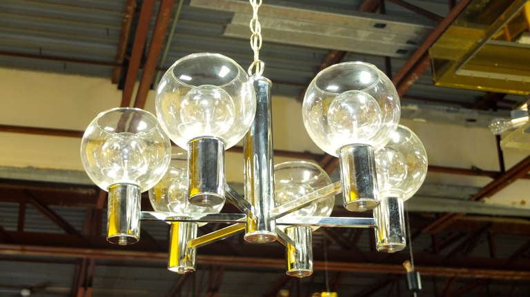 Lampadario moderno vintage degli anni '70 in cromo forse di Lightolier. Sei bracci si estendono da un mozzo centrale e terminano in cilindri cromati.  con in mano grandi paralumi a sfera in vetro chiaro con la parte superiore aperta.  Prese a vite