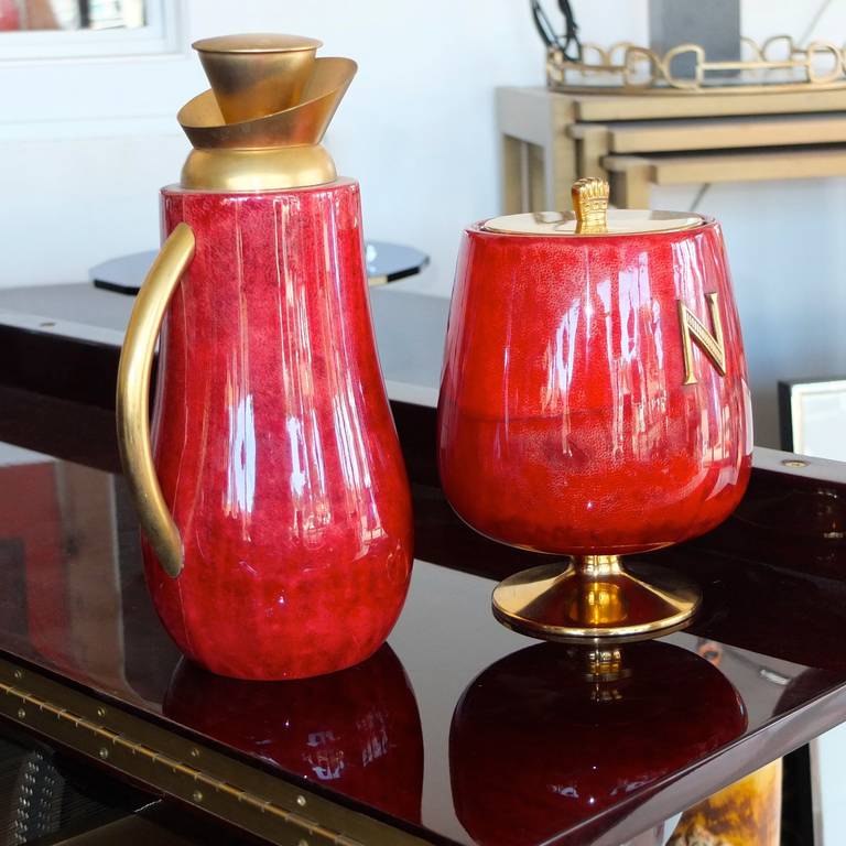 Aldo Tura footed ice server with lid and mercury glass lined carafe, both in tomato red dyed lacquered goatskin with gilt brass hardware and embellishments.

Ice bucket is 8
