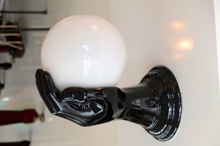 Vintage 1970s Italian ceramic wall lamp in form of a glossy black hand holding a glossy white glass globe with two inch opening on top. Clearly in the style of Fornasetti this is the largest one I've ever seen, nearly twice life size.  Takes a