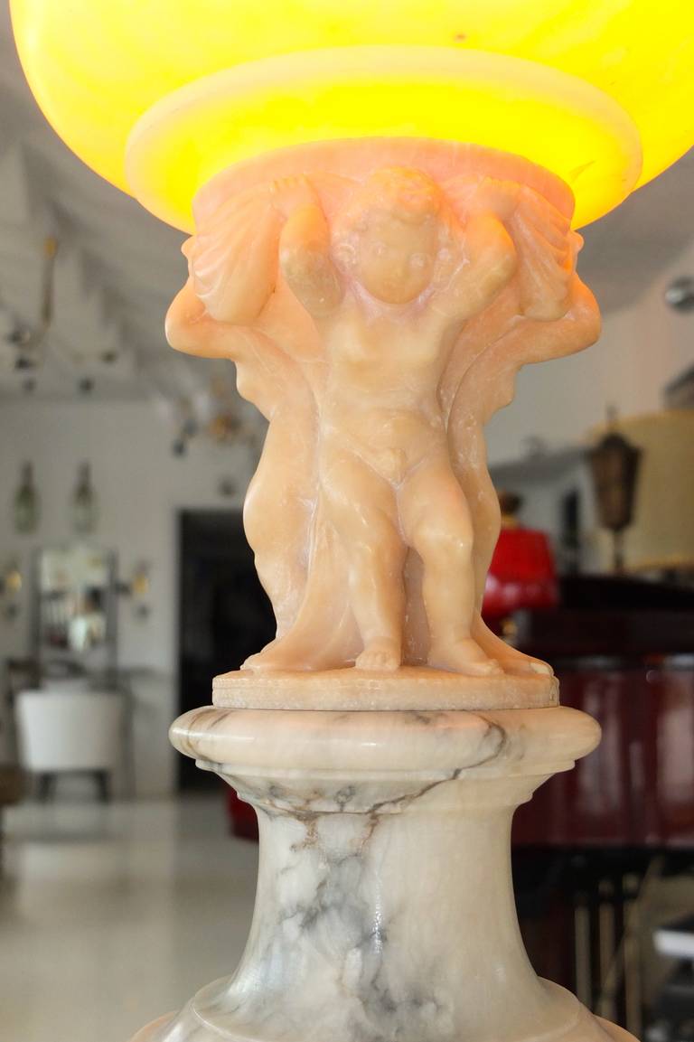 Late teens, early 1920's Italian alabaster lamp from the carving workshops of Volterra.

Lamp is in the form of three cherubini or putti supporting an oblong alabaster globe, illuminated from within.

The group stands on a round plinth which