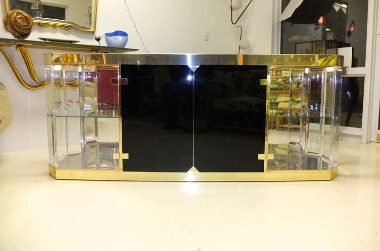 Elongated octagonal lucite sideboard / buffet / vitrine designed by Italian Antonio Pavia circa late 1970's with opulent brass and reflective chrome trims and details.  Pair of black acrylic center doors open to a single cupboard with one horizontal