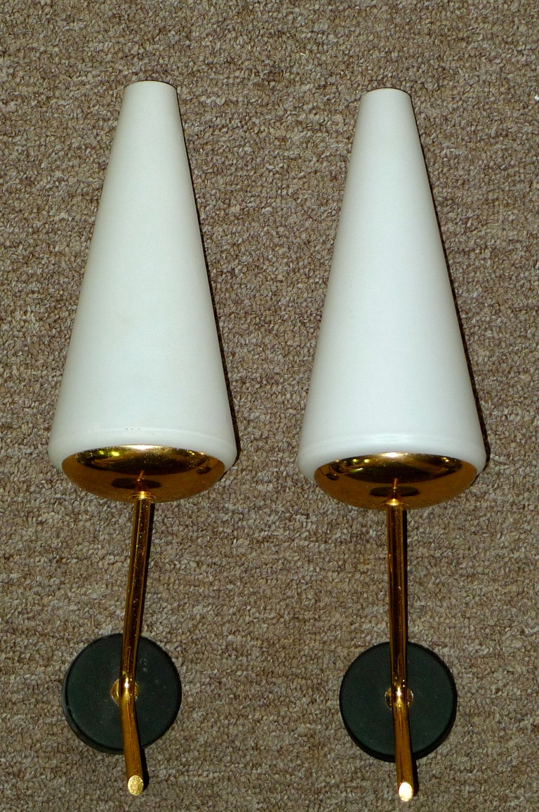 Coppia di applique moderniste francesi degli anni '50 in ottone con paralumi opalini a forma di cono e attacco a parete in metallo annerito.  Lampadina singola.  Ricablata.  Semplicemente elegante e chic.