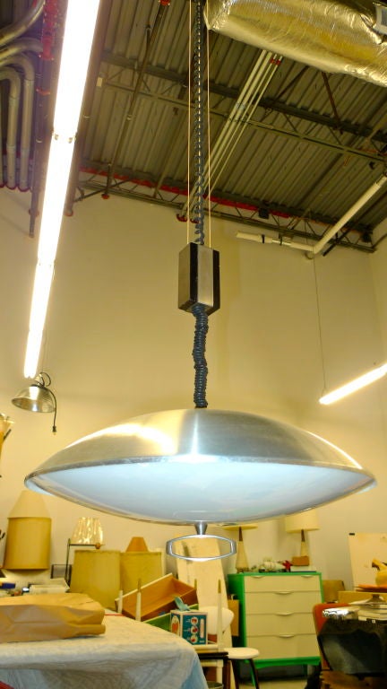 Signed Stilnovo UFO flying saucer shaped pendant light made of spun aluminum with an opaque white plexi reflector secured by a sculptural cast aluminum bottom finial suspended by a height adjuatable cloth covered curly cord weighted by a block of