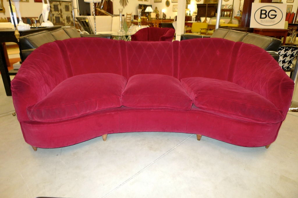 Lovely curved-back form with signature diamond-shaped welting and down seat cushions. Wood legs, dark red velvet upholstery, sofa: 85