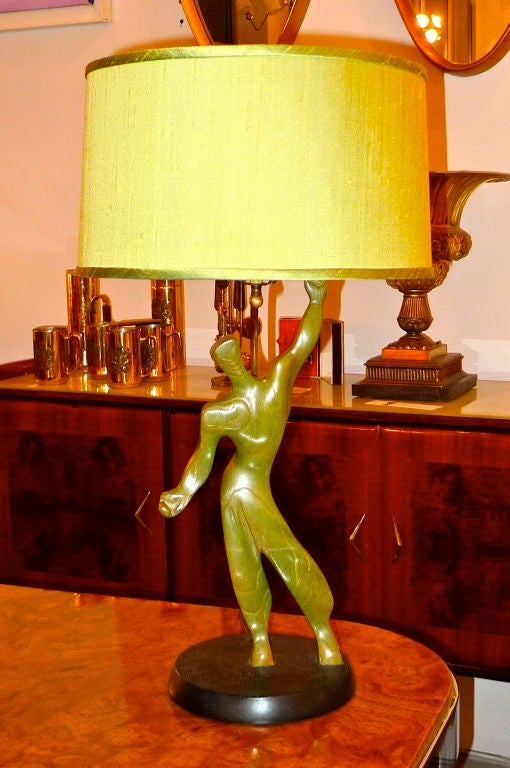 Whimsical table lamp with the figural modernist sculpture of a man in carved green washed wood on an ebonized base.  New pea green silk shade.
