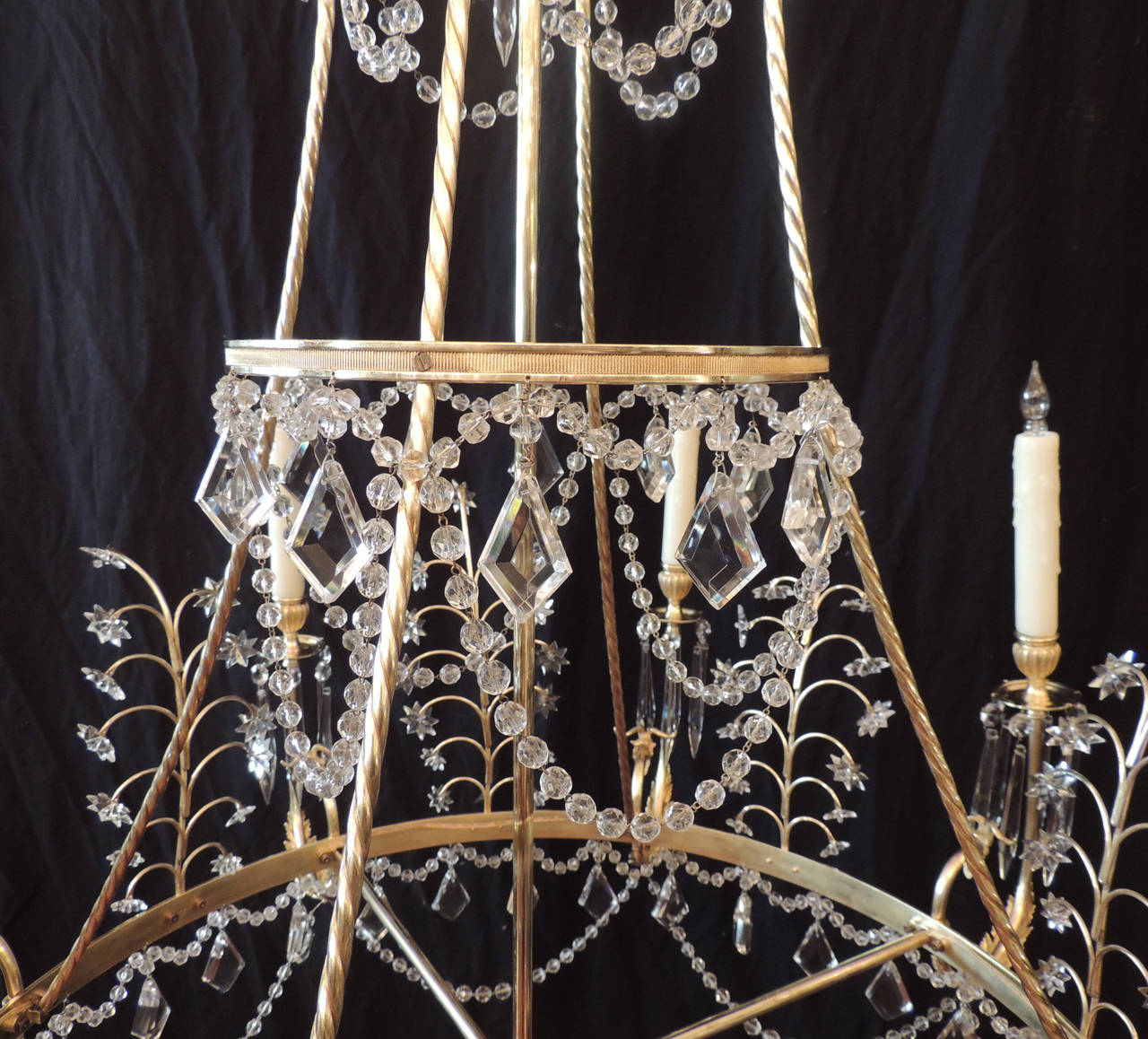 This chandelier was made in the first half of the 20th century in the Baltic States of Europe. This chandelier features three graduated rings decorated with crystal swags, French drops, and rosettes and one bottom ring that supports a crystal ball.