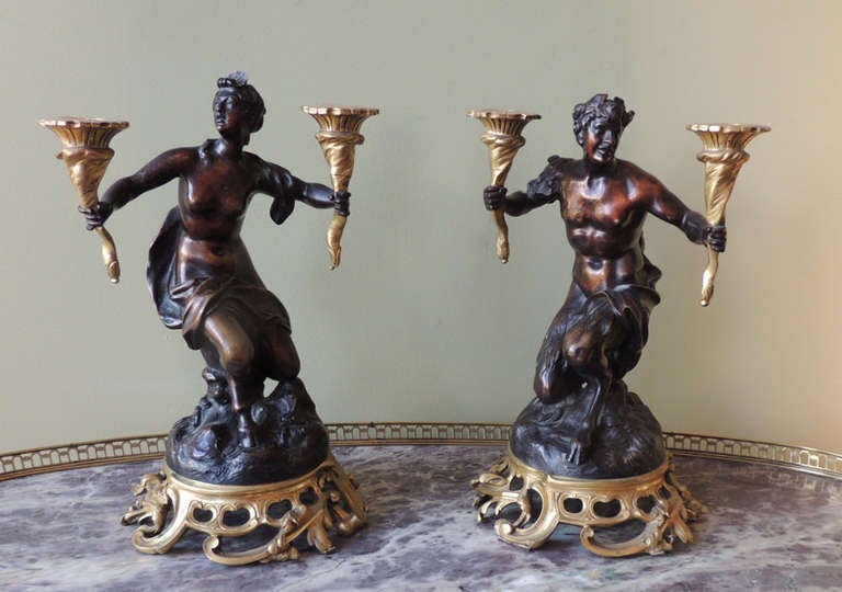 This pair of candelabras were made in France during the first half of the 18th century. These unique candelabras are statuettes in the form of male and female satyrs. Each of the statuettes holds bronze candle holders resembling torches. The bases