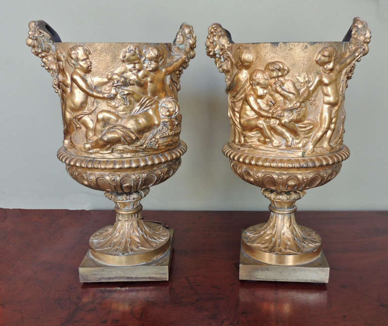 This pair of wine coolers was made in France during the mid-18th century. They are cast of bronze dore with putti figures. The handles on each side of the pieces are in the shape of arrangements of grapes. The wine coolers are each on a decorated