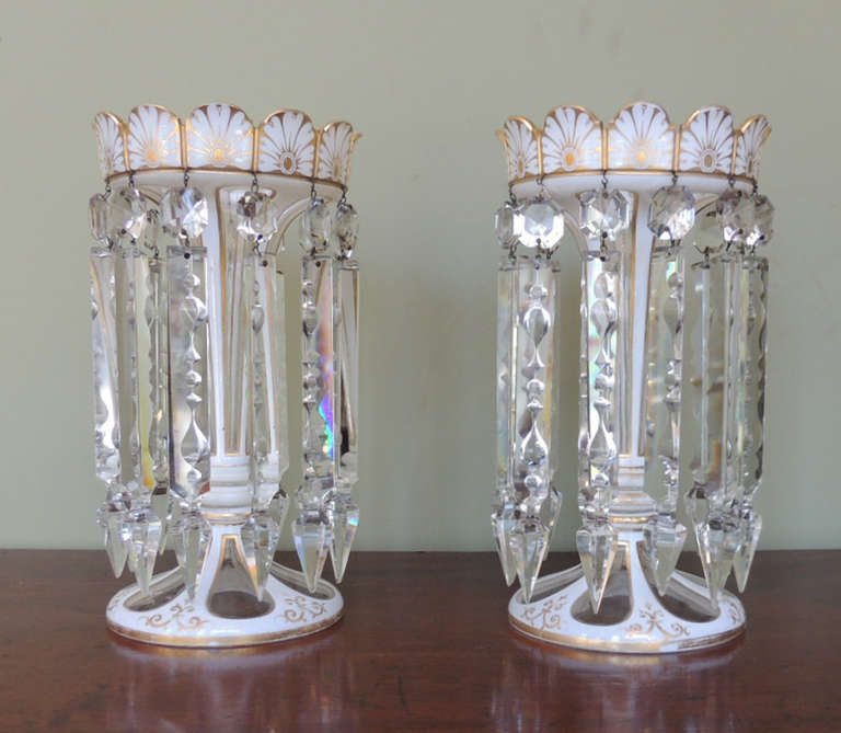 This pair of lusters were made in England during the first half of the 19th century. The body is made of cut-glass with applied gilt. There are twelve long prisms that hang from the top rim.