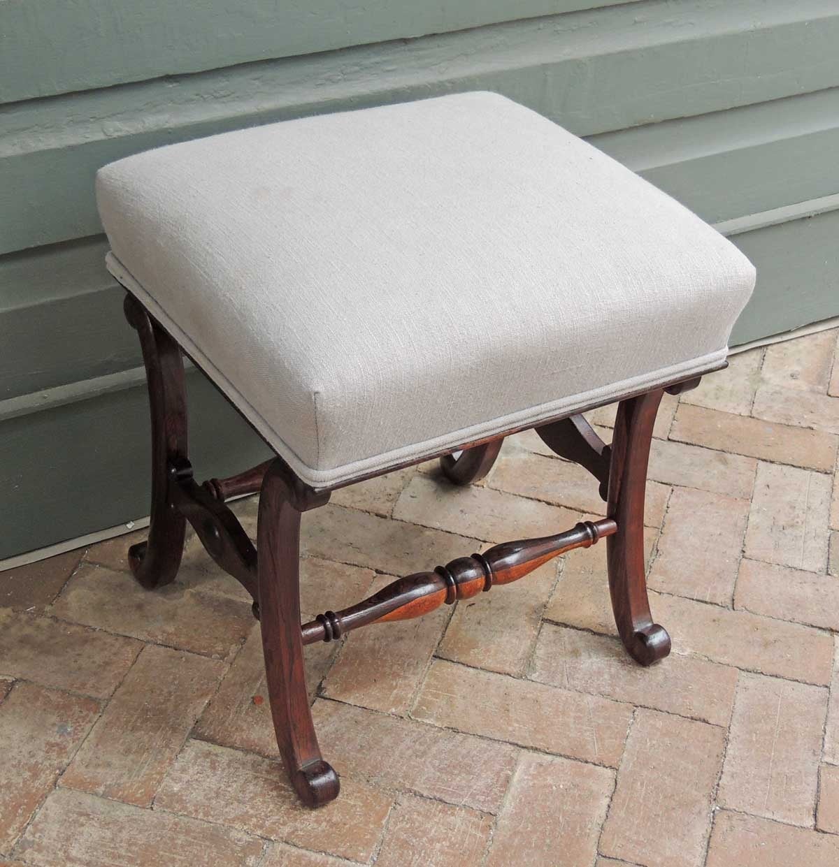 This wonderful stool was made in England during the first half of the 19th century. This stool has a recently reupholstered grey seat above scroll legs with carved side stretchers. There are two hand-turned center spindles made of rosewood and